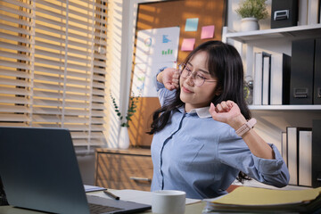 A young Asian woman poses in pain and stretches lazily after working too hard in the office. Office...
