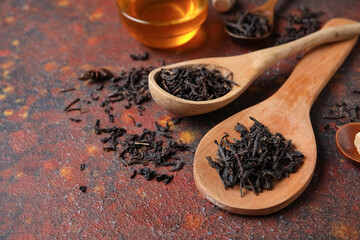 Wooden spoons with dry black tea leaves and glass bowl of honey on dark background, closeup