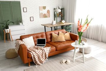 Folding screen, comfortable sofa, table and vase with gladiolus flowers in interior of living room