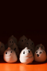 Ghost-shaped meringues with hand-drawn face on an orange background against a dark, moody background, creating a fun yet eerie atmosphere for Halloween treats.
