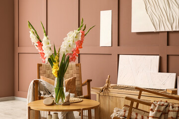 Wicker armchairs, table and vase with gladiolus flowers in interior of living room, closeup