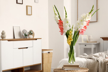 Books and vase with beautiful gladiolus flowers on wicker table in interior of bedroom, closeup