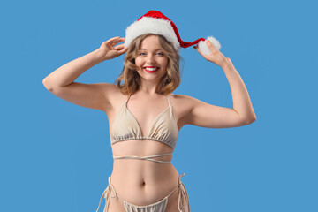Attractive young woman in swimsuit with Santa hat on blue background. Christmas celebration