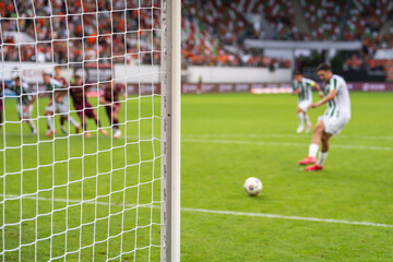 Detail of goal's post with net and football player during penalty kick in the background.