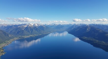 Aerial view of a vast lake with mountains reflecting in the calm water under a clear blue sky