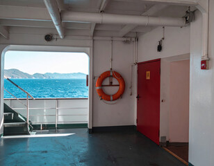 Interior Deck of a Modern Ferry Boat Featuring an Open Door View of the Deep Blue Ocean and Rugged Coastal Mountains; Travel Transportation, Nautical Lifebuoy Safety Ring