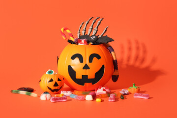 Cauldrons in shape of pumpkin with candies for Halloween and skeleton hand on orange background