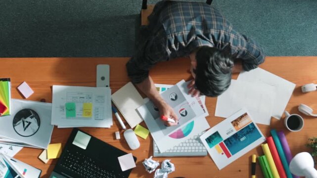Top view of designer writing and designing logo graphic at meeting. Closeup of business man working on colored palettes and writing idea on sticky notes on table with equipment and paper. Symposium.