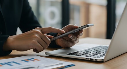 Business professional using smartphone with laptop and charts
