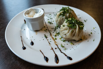 two steaming dumplings topped with chopped herbs are placed on white plate, alongside small bowl creamy sauce, creating tempting dish. close up.