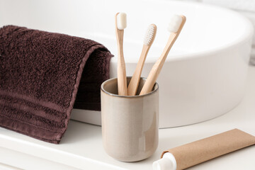 Cup with toothbrushes, toothpaste and towel on table in bathroom, closeup