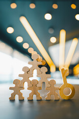 Wooden human figures stacked in pyramid with a key beside them, symbolizing teamwork, leadership,...
