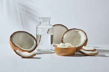 Clean white backdrop with coconuts, glass bottle and bowl of cream. Minimalist visual designed for fresh and modern cosmetic campaigns. Copy space