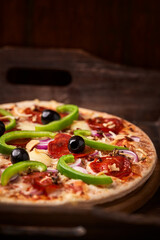 Pizza with chorizo ​​sausage, mozzarella cheese, green pepper and black olives. Rustic wooden background. Soft focus.	
