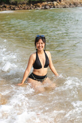 Asian woman is happily playing in the sea amidst the waves, smiling brightly.