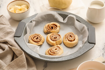 Baking tray with raw cinnamon buns on marble background, closeup