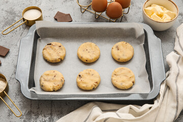 Baking tray with raw cookies and ingredients on grey grunge background