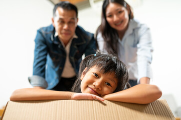 Family's Moving Day: An adorable girl and her parents gather around a cardboard box, with the child beaming at the camera, hinting at a new beginning filled with possibilities and joy.
