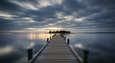 Wooden pier extending towards a small island with reflective water under a dramatic cloudy sky