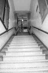 Black and white view of a rustic staircase in Puebla, Mexico, leading to a wrought iron gate, capturing everyday life in a historic urban setting.