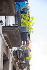 Upward view of traditional Mexican balconies with wrought iron railings, classic lanterns, and potted plants, captured on a sunny day in a relaxed, touristic urban setting.