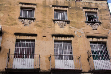 Weathered yellow building in Puebla, Mexico, with faded ornate balconies and rustic textures, revealing the beauty of its historic past.