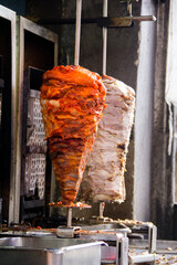 Cinematic close-up of two vertical meat spits in Puebla, Mexico: vibrant red al pastor and succulent white pork for tacos &aacute;rabes, glistening under natural daylight a classic Mexican street food.