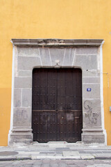 Historic wooden door framed by carved stone on a vibrant yellow wall in Puebla, Mexico. Traditional architecture, cultural heritage, and colorful urban identity.