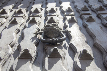 Black and white close-up of a colonial wooden door with flowing wood grain, metal studs, and a lion-head door knocker, symbolizing strength, craftsmanship, and historic elegance.