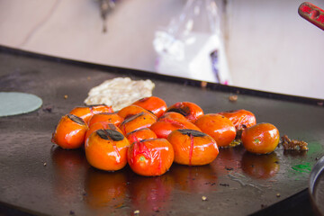 Close-up of red tomatoes roasting on a metal griddle at a Mexican street food stall, showing charred skins and preparation for authentic red salsa.