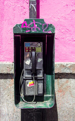 Vandalized old phone booth in Latin America, covered in colorful graffiti, captured in dramatic hard light, reflecting urban street culture and social issues.
