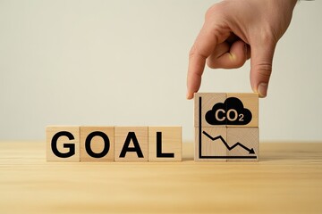 Hand places co2 reduction goal block next to word goal with downward trend graph
