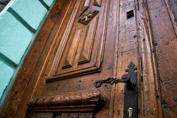 Rustic colonial door in Mexico, featuring decorative ironwork, polished aged wood, and a striking turquoise stone frame.