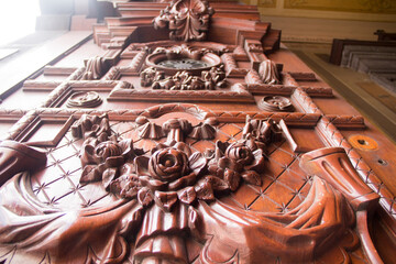 Colonial wooden door with intricate floral carvings, antique emblem, and unique fish-shaped knockers, reflecting historic Mexican Baroque craftsmanship.