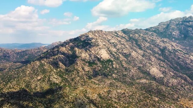 An aerial perspective showcases the stunning, rocky terrain of the Latmos Mountains, also known as Mount Beşparmak, under a bright blue sky with scattered clouds. This footage captures the natural bea