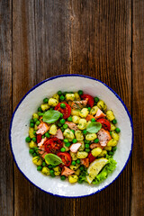 Gnocchi with salmon bites, green peas and cherry tomatoes on wooden table. Top view