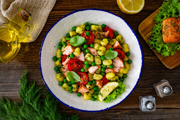 Gnocchi with salmon bites, green peas and cherry tomatoes on wooden table. Top view