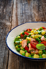 Gnocchi with salmon bites, green peas and cherry tomatoes on wooden table	