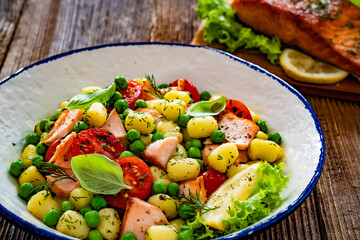 Gnocchi with salmon bites, green peas and cherry tomatoes on wooden table	