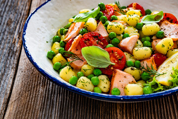 Gnocchi with salmon bites, green peas and cherry tomatoes on wooden table	