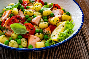 Gnocchi with salmon bites, green peas and cherry tomatoes on wooden table	