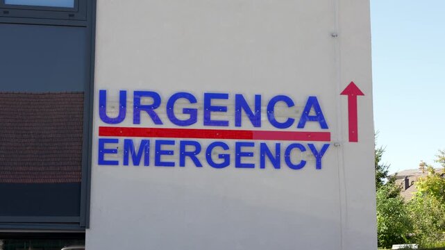 Emergency department sign on hospital wall with direction arrow showing way to urgent medical care entrance.