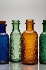Assortment of tall colored glass bottles in shades of amber, cobalt blue, emerald green, and ruby, arranged in a row on a white background, vibrant yet elegant,Generative Ai
