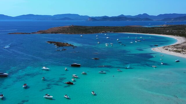 Espalmador island featuring white sand beaches, clear turquoise water, and anchored boats. Ibiza and the island of Es Vedra in the background. Magic aerial view flight