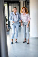 Fototapeta premium Two businesswomen laughing together in modern office hallway