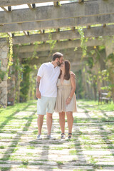 Fototapeta premium A man and woman are kissing in a garden. The woman is wearing a dress and the man is wearing shorts