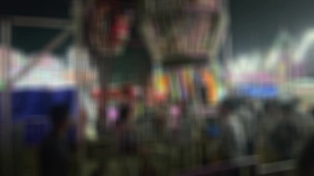 Colorful blurred night shot of a big lighted Ferris wheel in an Indian funfair park, with an abstract blurred background of people gathering and shopping at the local city night market
