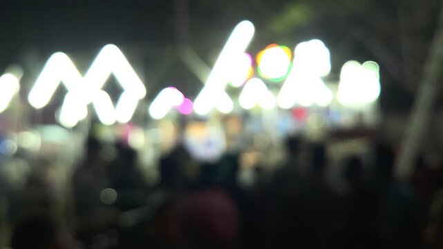 Colorful blurred night shot of a big lighted Ferris wheel in an Indian funfair park, with an abstract blurred background of people gathering and shopping at the local city night market