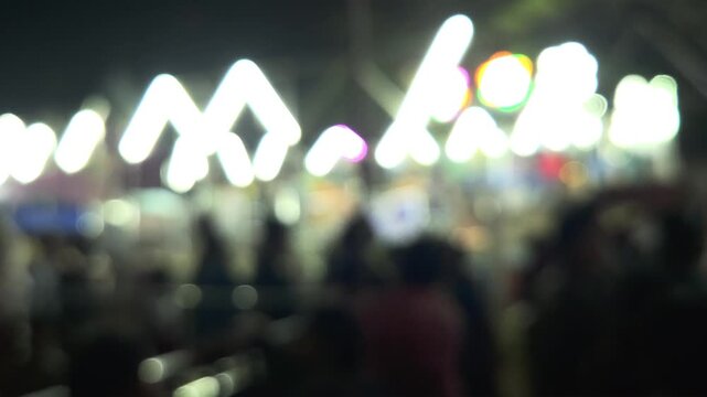 Colorful blurred night shot of a big lighted Ferris wheel in an Indian funfair park, with an abstract blurred background of people gathering and shopping at the local city night market