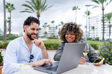 Diverse couple working on laptop outdoors enjoying leisure